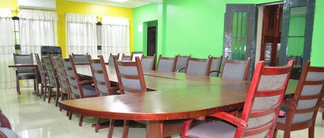 A conference room with a large wooden table surrounded by chairs, yellow and green walls, and a door with a window.