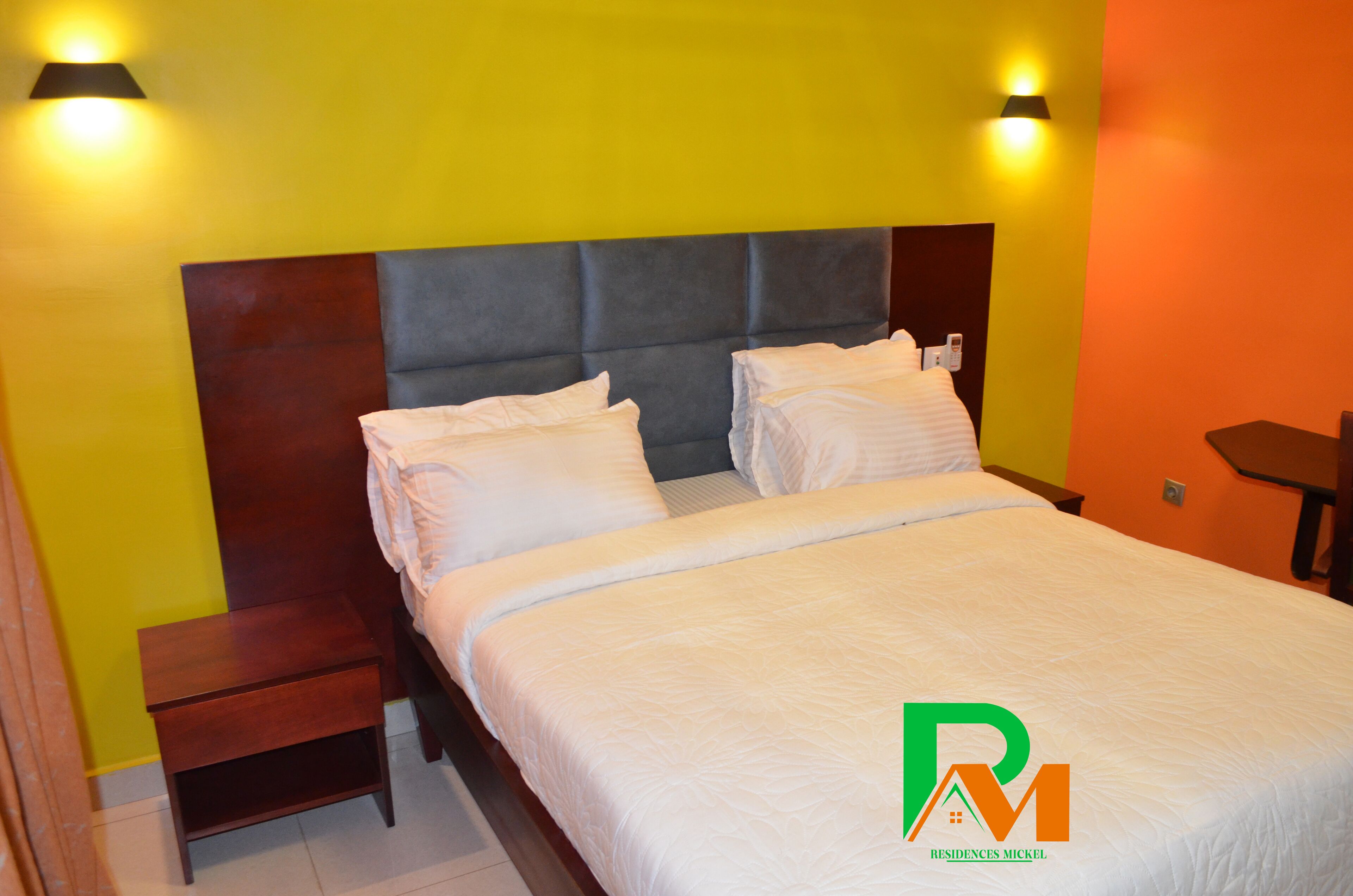 Una habitación de hotel con cama, mesitas de noche y dos lámparas fijadas a la pared.