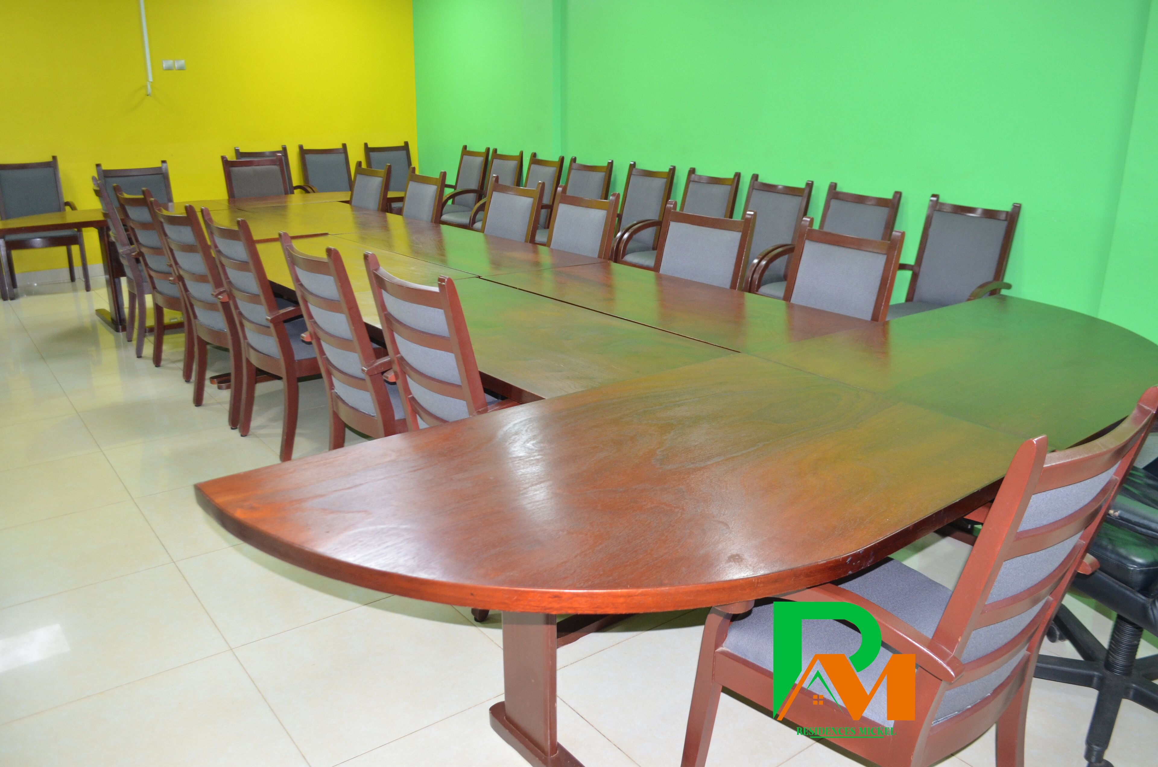 A conference room with a large oval table surrounded by chairs, a yellow wall, and a green wall.