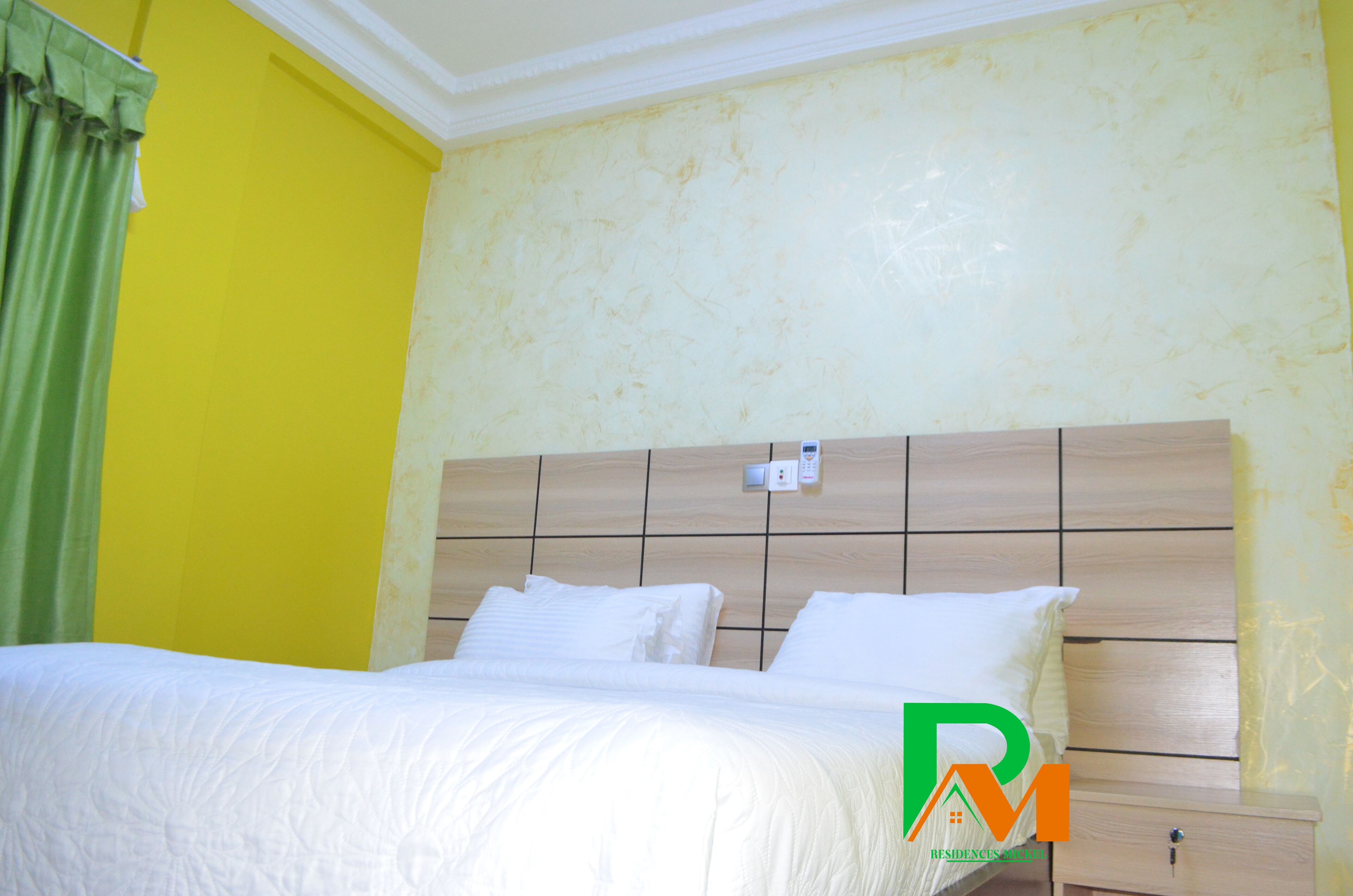 A hotel room with a bed, a nightstand, and a wall-mounted electrical outlet.