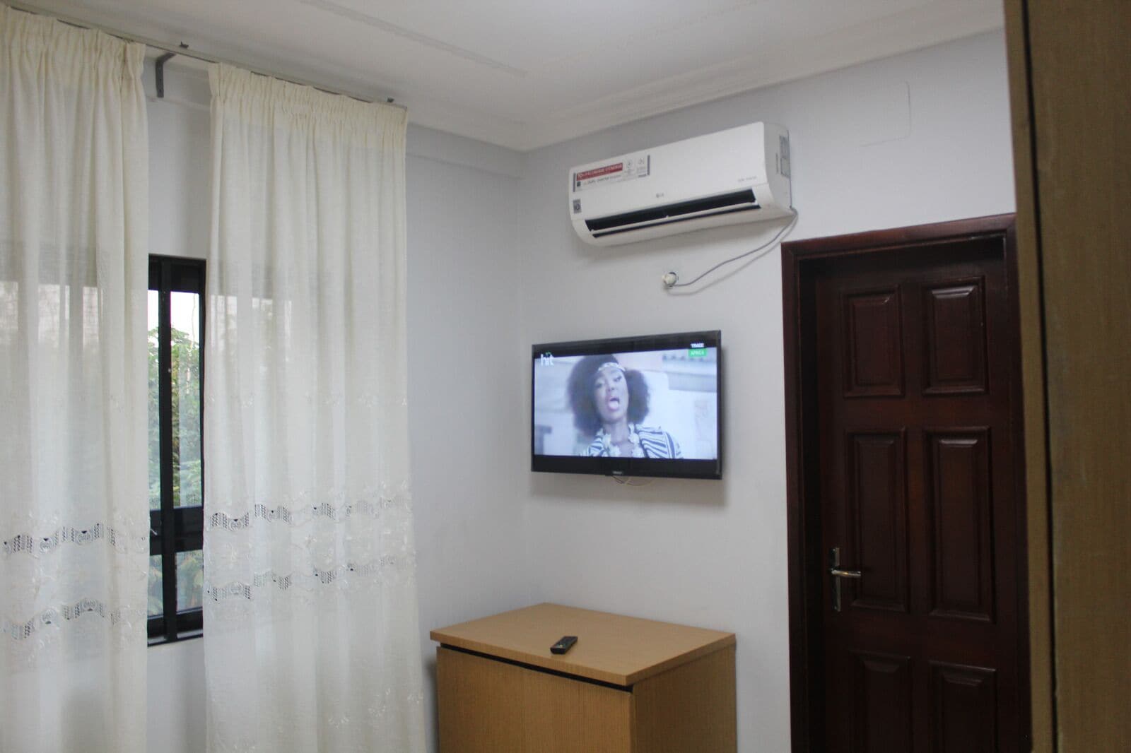 Une pièce avec un bureau en bois, un téléviseur fixé au mur et une fenêtre avec des rideaux.