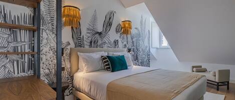 A modern bedroom with a sloped ceiling, a large bed with white bedding, a wooden side table, and a wall with black and white leaf patterns.
