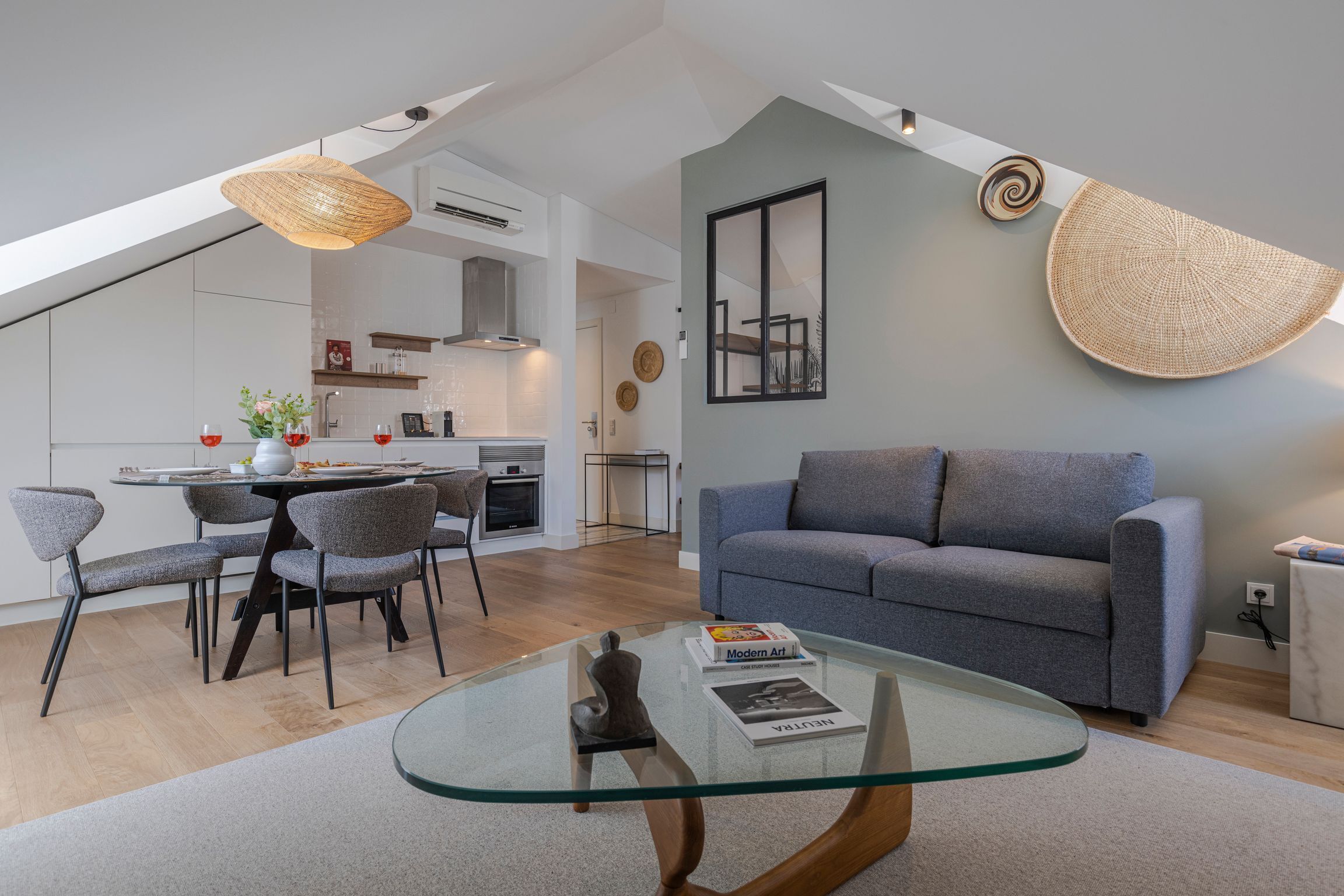A modern living room with a glass coffee table, grey sofa, and dining area with chairs.