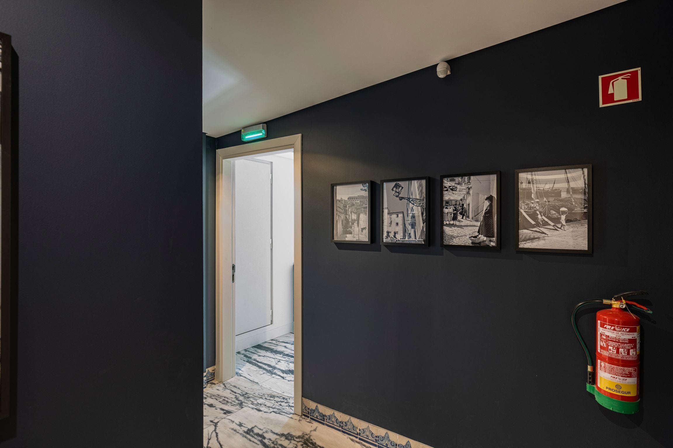 En gang med en mørk væg, en brandslukker og tre indrammede fotografier.