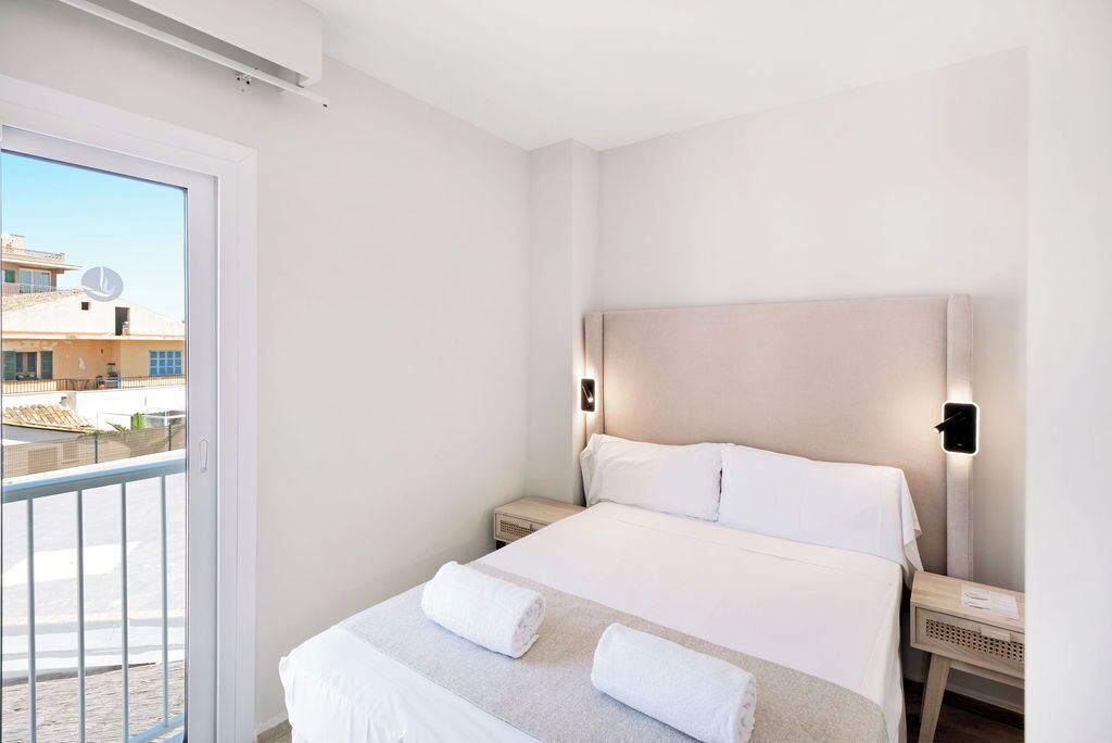 Habitación de hotel con una cama grande, dos mesitas de noche y un balcón con vistas a edificios.