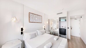 Una habitación de hotel moderna con una cama grande, mesitas de noche, un armario, un espejo y una pequeña cocina.