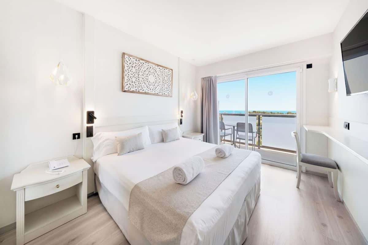 Ein Hotelzimmer mit einem großen Bett, einem Schreibtisch, einem Stuhl und einem Balkon mit Meerblick.