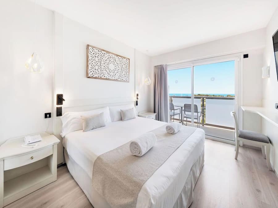 Habitación de hotel con una cama grande, un escritorio, una silla y un balcón con vistas al mar.