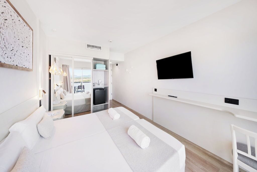 Una habitación de hotel moderna con una cama, un televisor montado en la pared y vistas al exterior.
