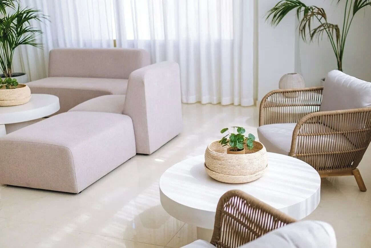 Een moderne woonkamer met een beige modulaire bank, een ronde witte salontafel en rieten stoelen.
