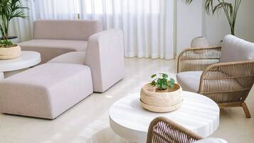 Een moderne woonkamer met een beige modulaire bank, een ronde witte salontafel en rieten stoelen.