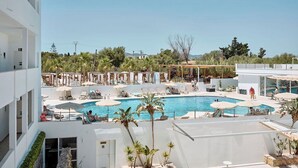 Zona de piscina en la azotea con múltiples tumbonas y sombrillas, rodeada de vegetación y un cielo despejado.