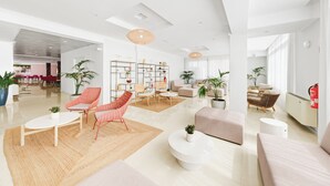 Un salón amplio y moderno con un sofá grande, una mesa de centro y una mesa de comedor. Hay varias sillas y una estantería con objetos decorativos.