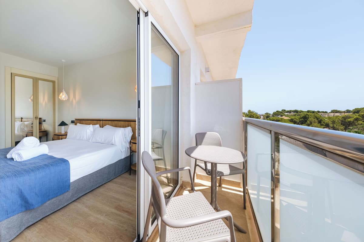 Ein Hotelzimmer mit Bett, einem Balkon mit Tisch und Stühlen und Blick auf die Landschaft.