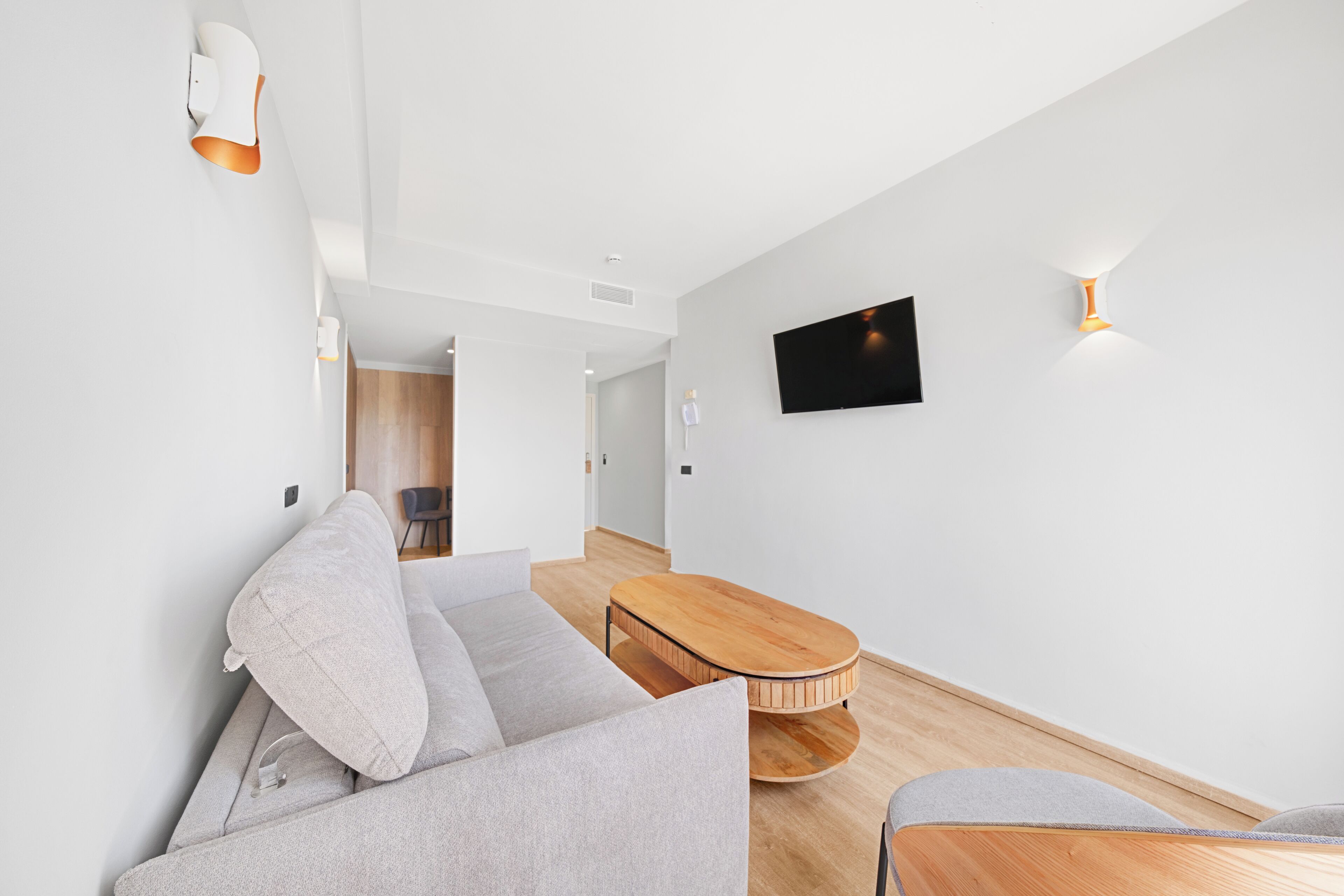 A modern living room with a grey sofa, a wooden coffee table, and a flat-screen TV mounted on the wall.