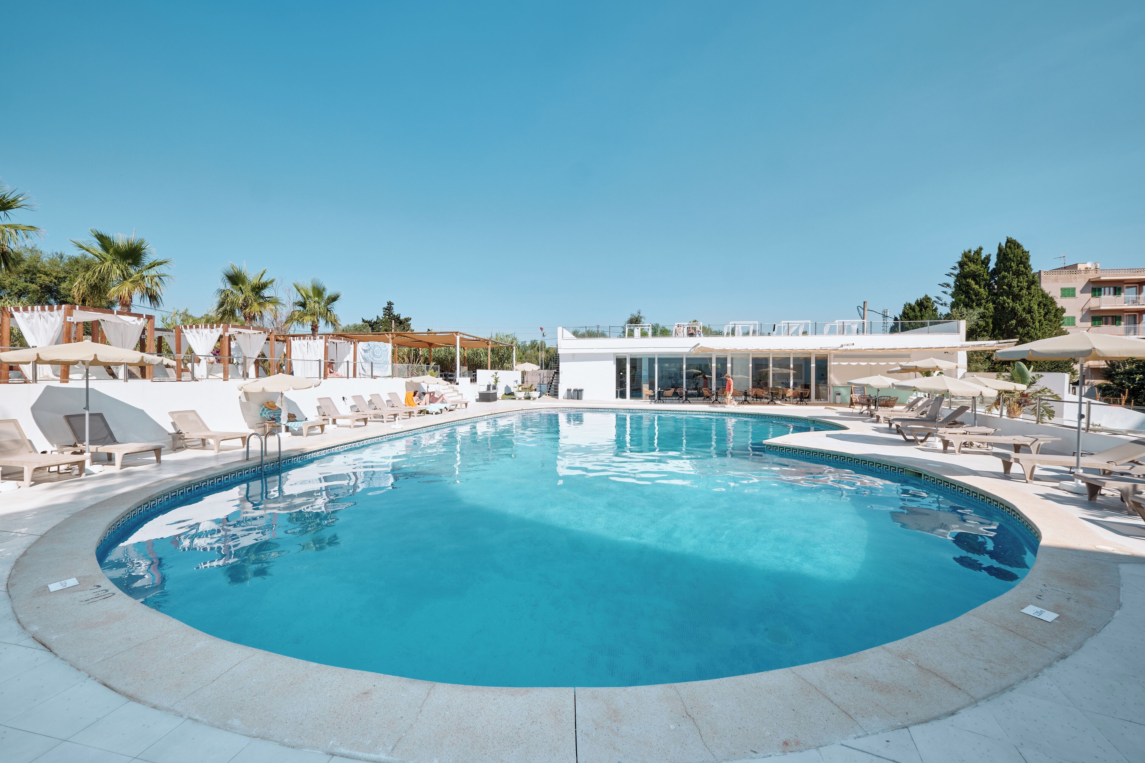 A swimming pool with lounge chairs and umbrellas, surrounded by palm trees and buildings.