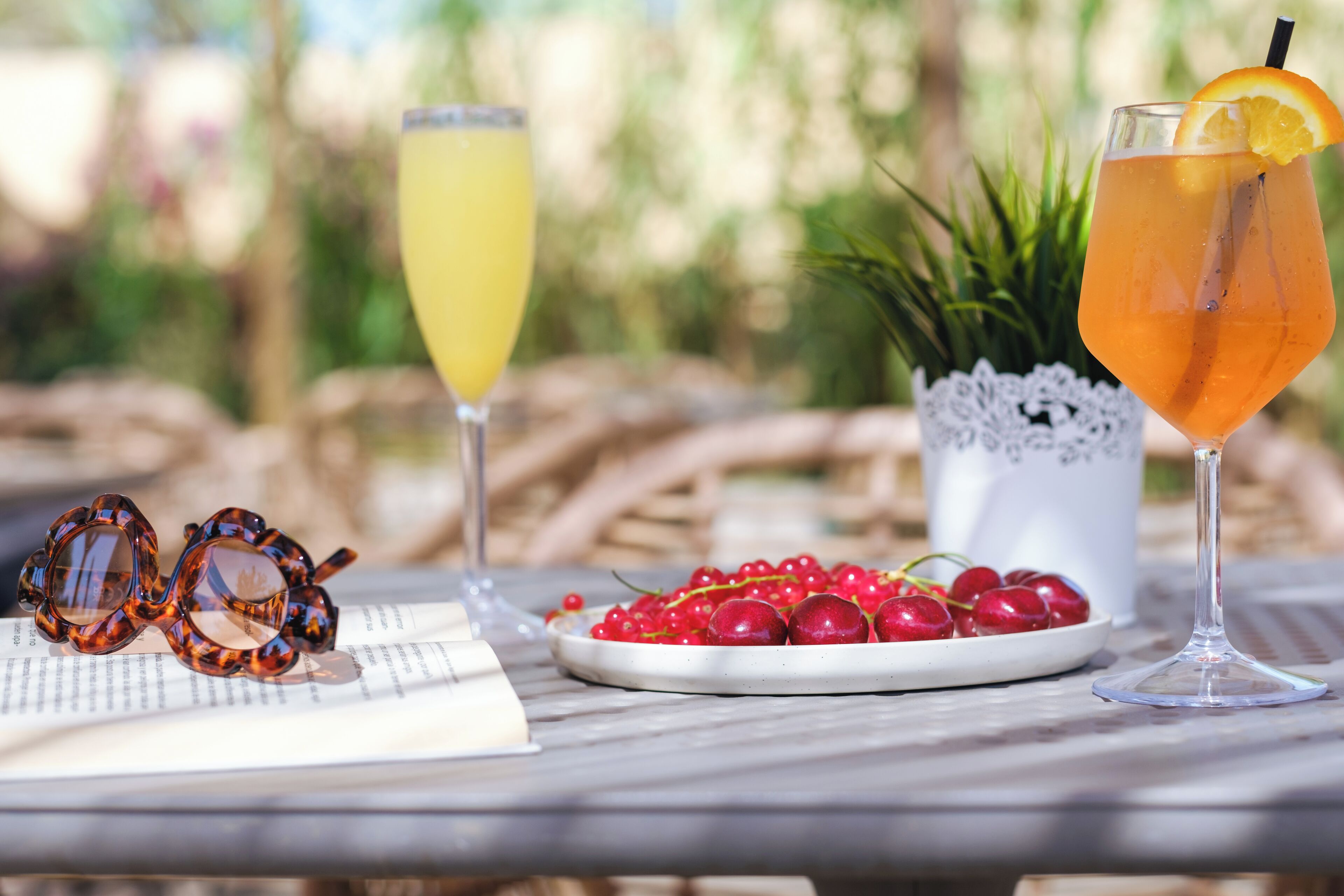 A table with two drinks, a pair of sunglasses, and a plate of red berries.