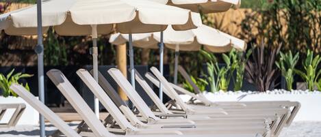 A row of sun loungers with beige umbrellas in a garden setting.