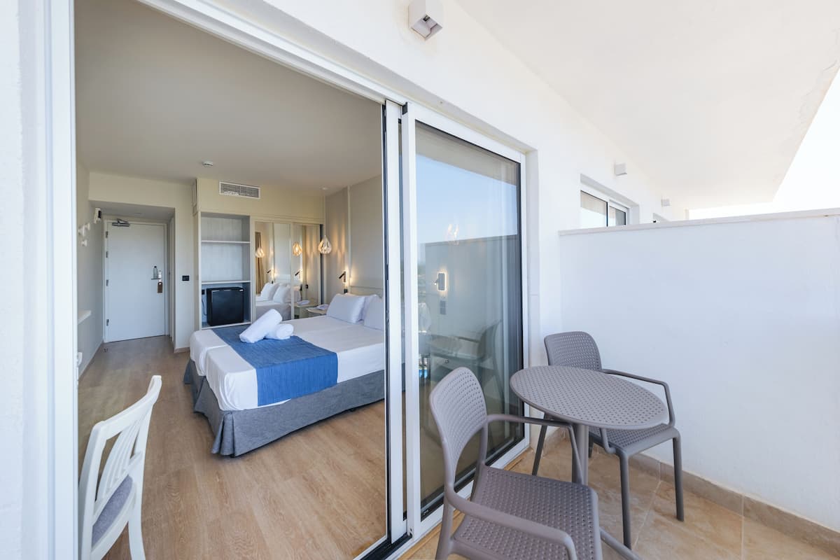 Ein Hotelzimmer mit einem Bett, einer Sitzecke mit Stühlen, einem Fernseher und einer Glasschiebetür, die auf einen Balkon führt.