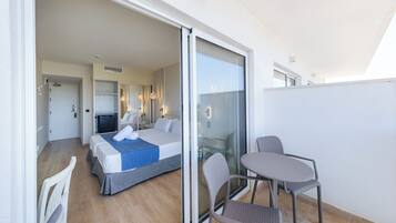 Habitación de hotel con cama, zona de estar con sillas, televisión y puerta corrediza de vidrio que da a un balcón.