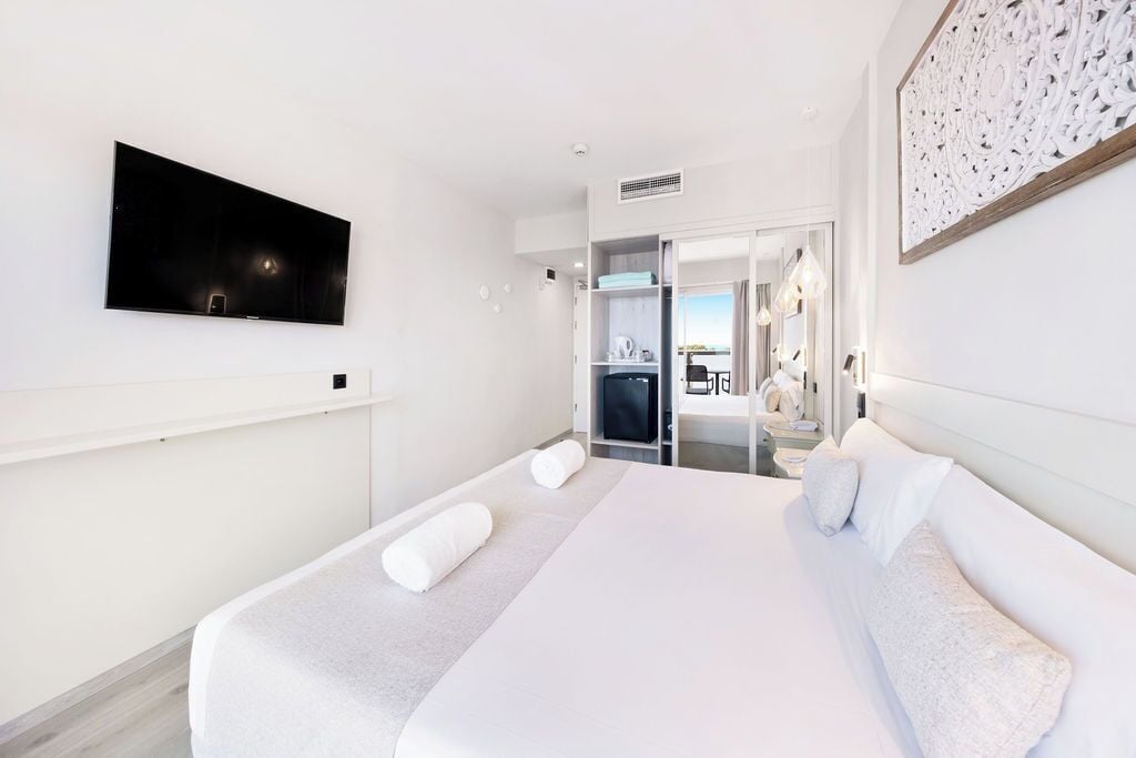 A modern hotel room with a large bed, a flat-screen TV mounted on the wall, and a walk-in closet with a mirror and shelves.
