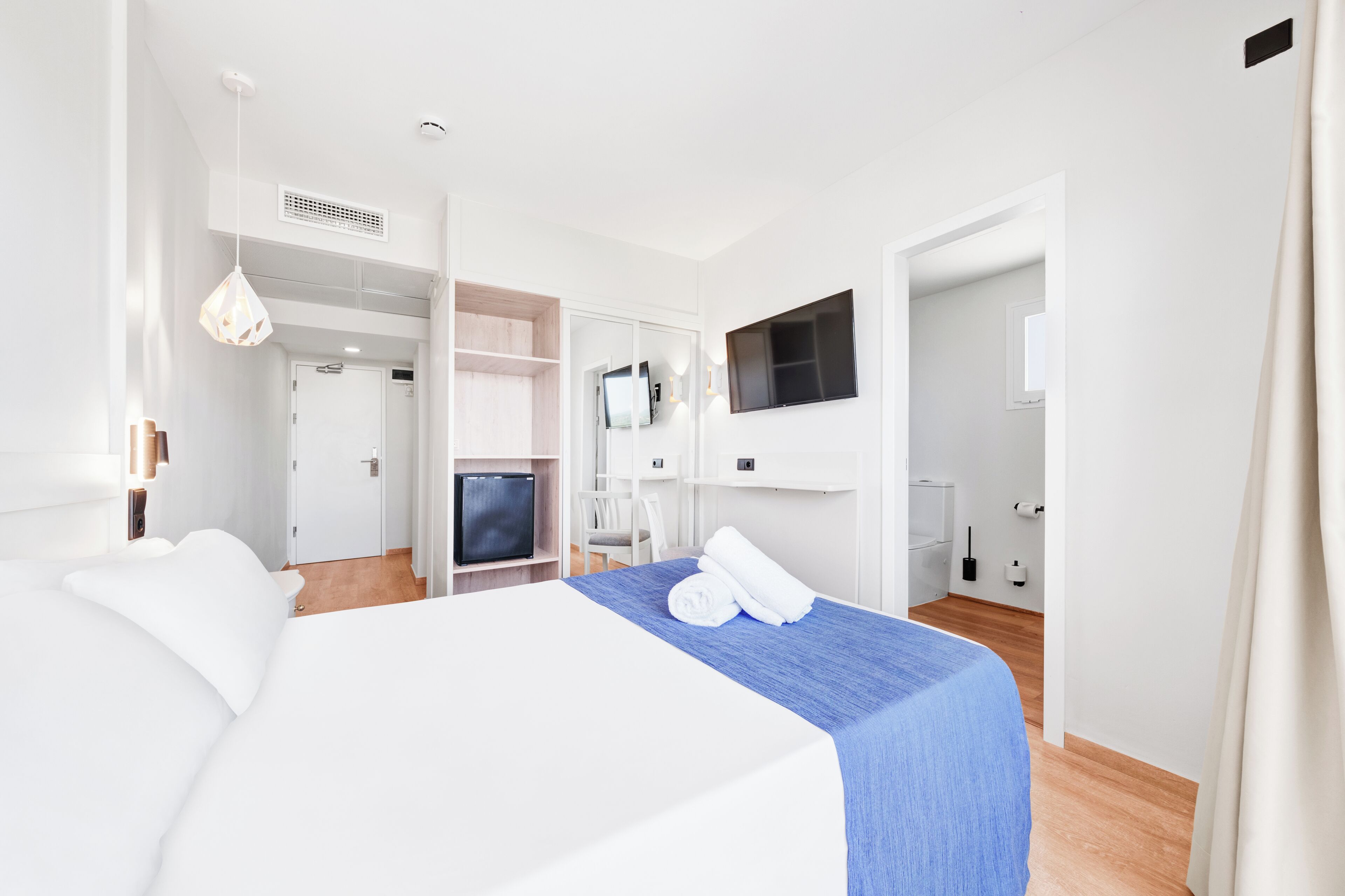 A hotel room with a large bed, a TV, a desk, and a wardrobe.