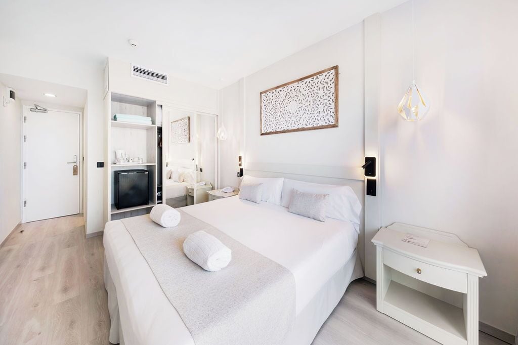 A modern hotel room with a large bed, a bedside table, a wardrobe, and a mirror.