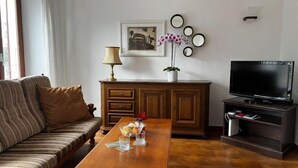Un saló amb un sofà, una taula de centre amb aperitius, una televisió i un moble amb una planta.