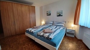 Un dormitori amb llit, armari de fusta, dues taules de nit amb làmpades i dos quadres penjats a la paret.