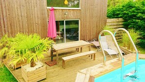 A wooden deck with a pool, a table, chairs, and a bench. - House with heated swimming pool 3 km from the beach (PLEUMEUR BODOU)