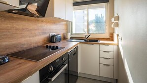 Eine kleine Küche mit einer Holz Arbeitsplatte, einem Einbauofen und einem Fenster mit Jalousien.