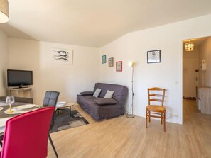 Ein modernes Wohnzimmer mit einem grauen Sofa, einem Esstisch mit roten Stühlen, einem Flachbildfernseher und einer Stehlampe.