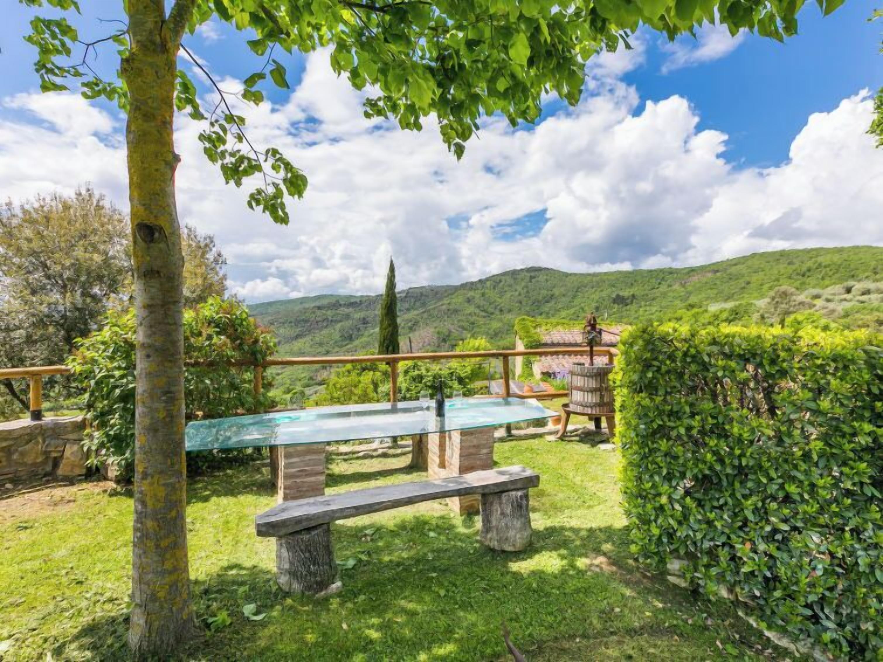 Une piscine entourée de parois de verre, avec un banc en bois, le tout agrémenté d’une végétation luxuriante et offrant une vue panoramique sur des collines verdoyantes.