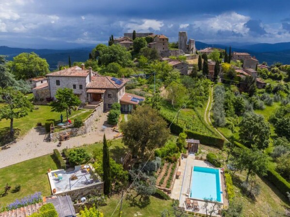 A villa with a swimming pool, surrounded by lush greenery and a historic stone building in the background.
