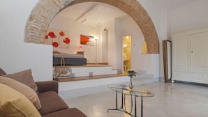 A spacious living area with a brown sofa, a glass coffee table, and a brick archway leading to a bedroom. - Lunaria + Solaria + Nuvola by Interhome (Ambra)