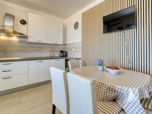 Une cuisine moderne avec des meubles blancs, une hotte de cuisinière en acier inoxydable, une machine à café et un téléviseur à écran plat fixé sur un mur à rayures.