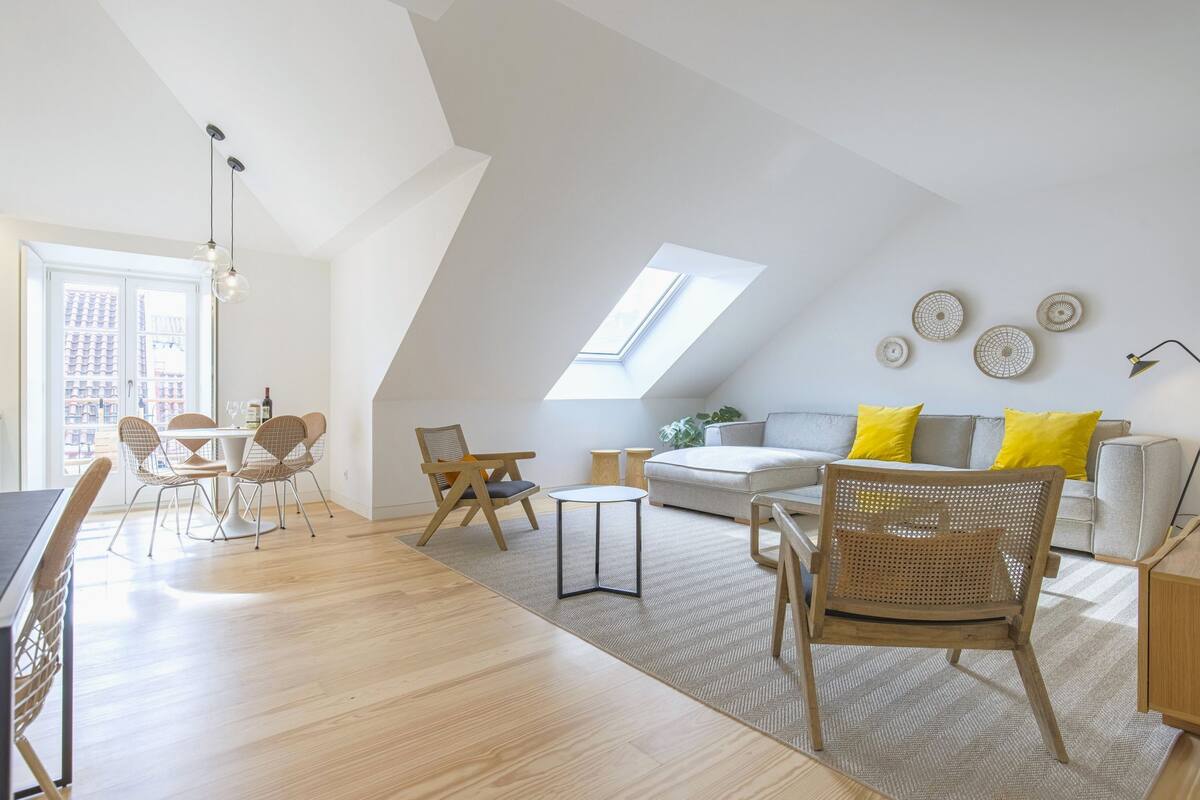 A modern loft apartment with a dining area, a living room with a sofa and yellow cushions, and a skylight.