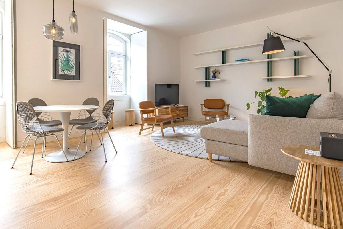 A modern living room with a round dining table, two chairs, a sofa, a TV, and a bookshelf.