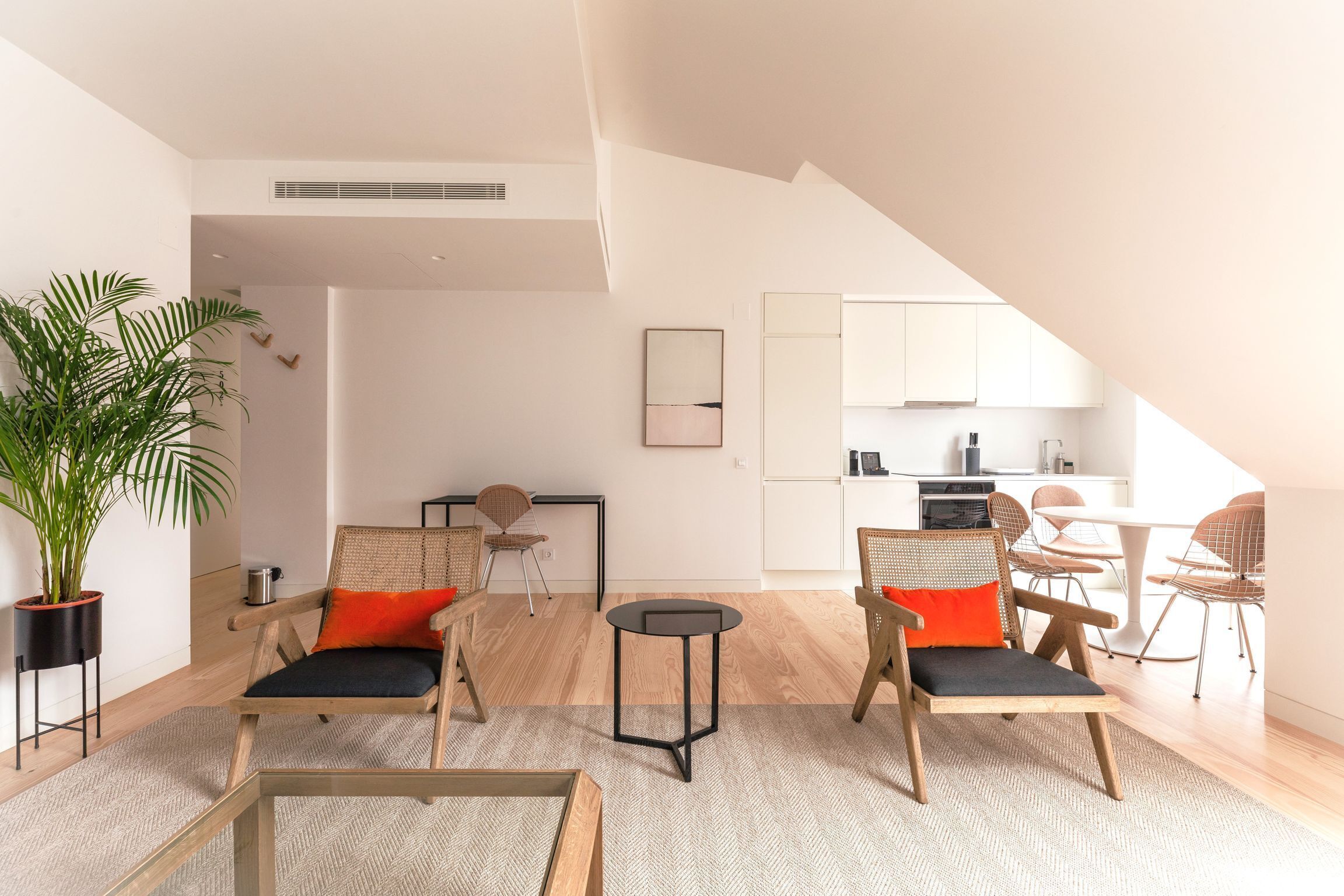 A modern living room with a dining area, kitchen, and a staircase leading to an upper level.