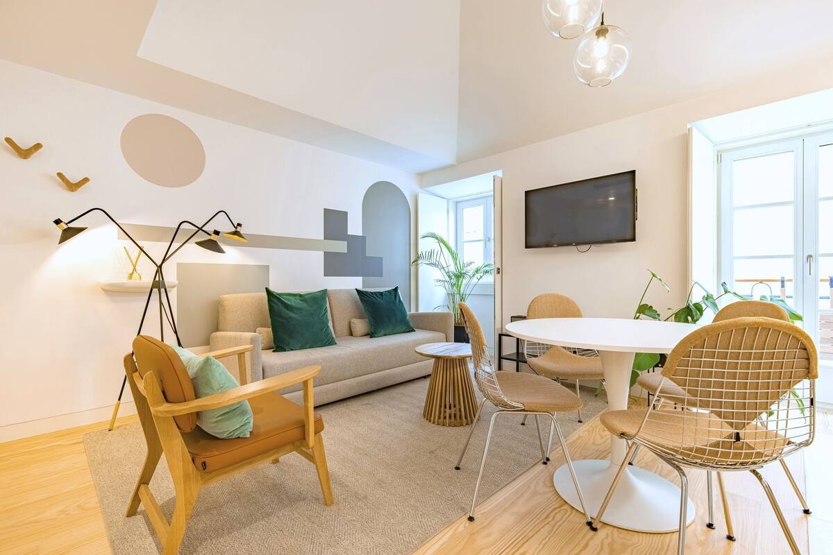 A modern living room with a sofa, chairs, a dining table, and a TV mounted on the wall.