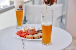 A glass of beer being poured into a tall glass, with a plate of snacks and a fork in the foreground.
