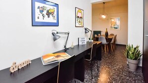 A modern office space with a long desk, two desks, and chairs. There are framed artworks on the walls, a potted plant, and a sign with the words "CITY VIBES APT".