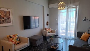 A modern living room with a flat-screen TV, two sofas, a coffee table, and a large window with sheer curtains.