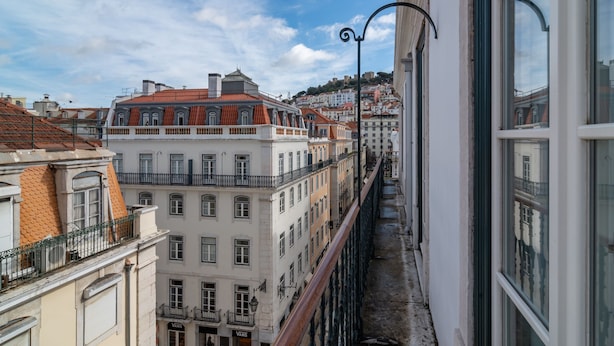 A narrow urban street with buildings on either side, featuring balconies and a clear sky.