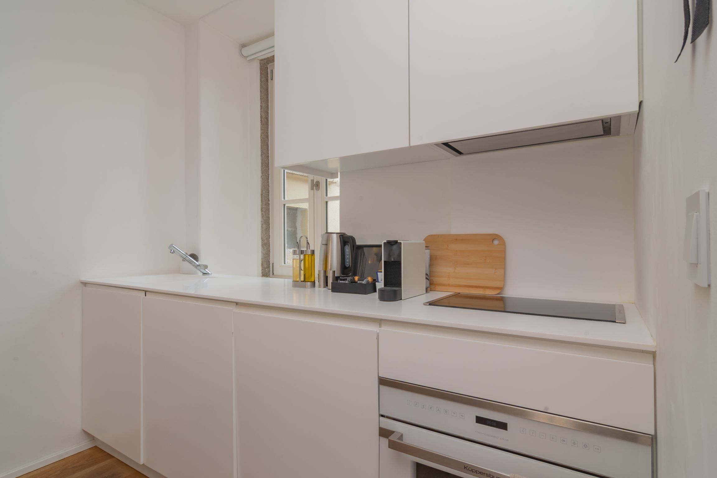 A modern kitchen with white cabinetry, a built-in oven, and a coffee maker on the countertop.