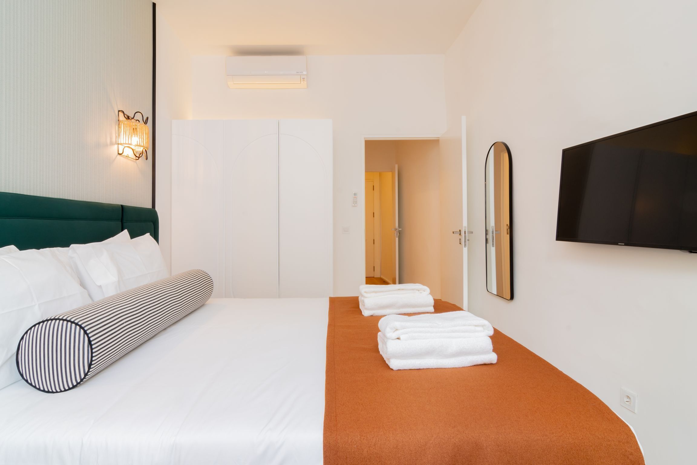 Habitación de hotel con cama, un espejo grande, televisor de pantalla plana y puerta de baño.