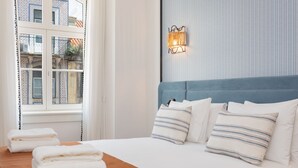 A neatly made bed with white linens and striped pillows, a blue headboard, and a wall-mounted light fixture.