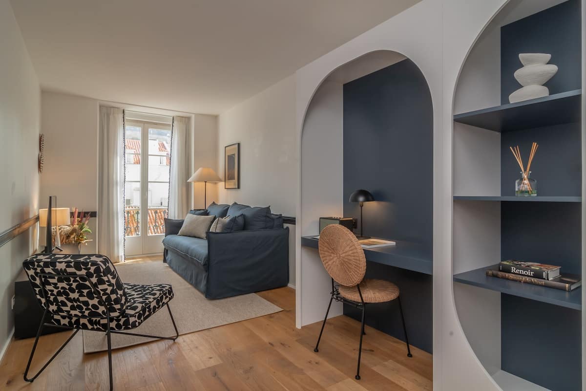 Una sala de estar moderna con un sofá, una butaca estampada, un escritorio y una estantería.