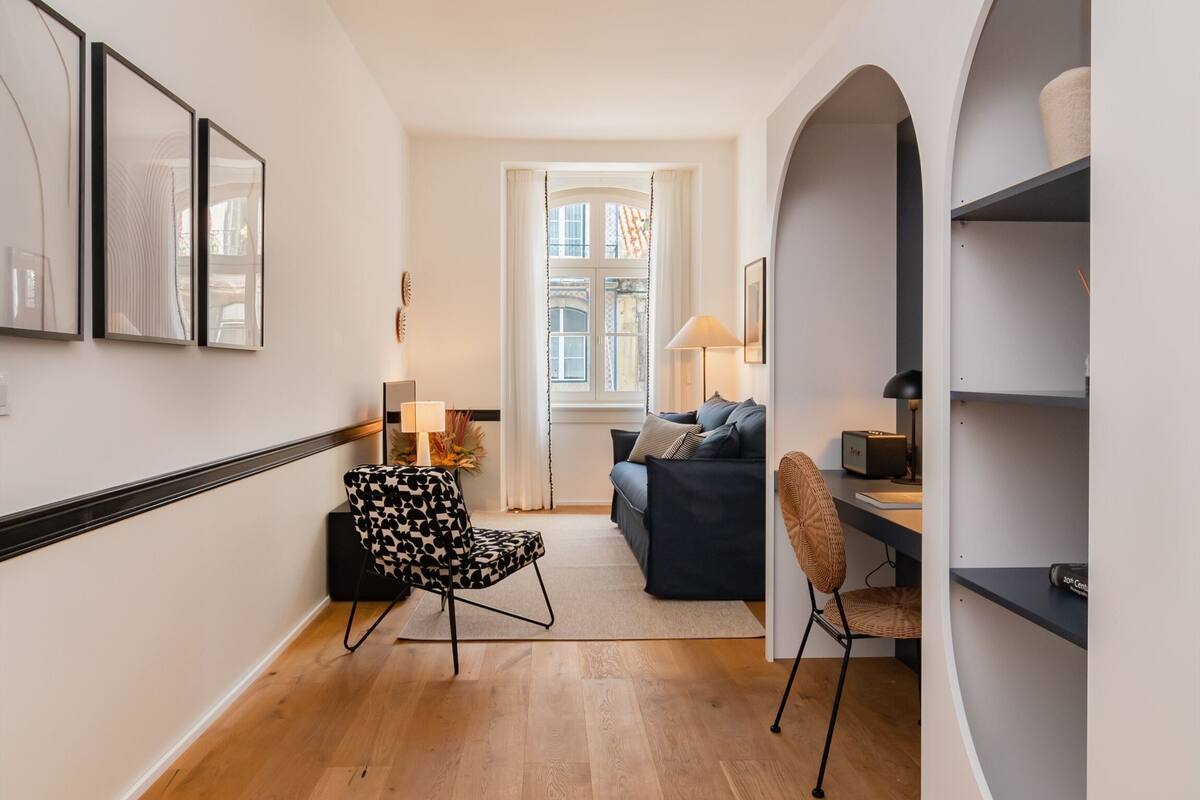 Una sala de estar moderna con un sofá, dos sillones, una lámpara y un ventanal con cortinas.