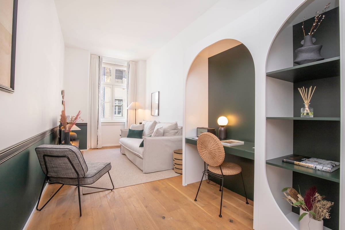 Una sala de estar moderna con un sofá, una silla, una mesa con lámpara y una estantería.